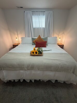 Un letto rifatto con una coperta bianca, due cuscini e un cesto decorativo con girasoli.