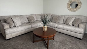 A living room with a sectional sofa, a round coffee table, a decorative vase, and a mirror on the wall. - Garden Estate at the base of the Mountains, sleeps 16, near BYU (Orem)