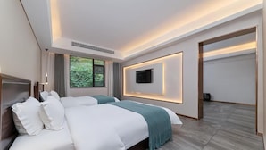 A modern hotel room with a large bed, a TV mounted on the wall, and a view of greenery outside. - Serene Peaks Courtyard (Xiangxi)