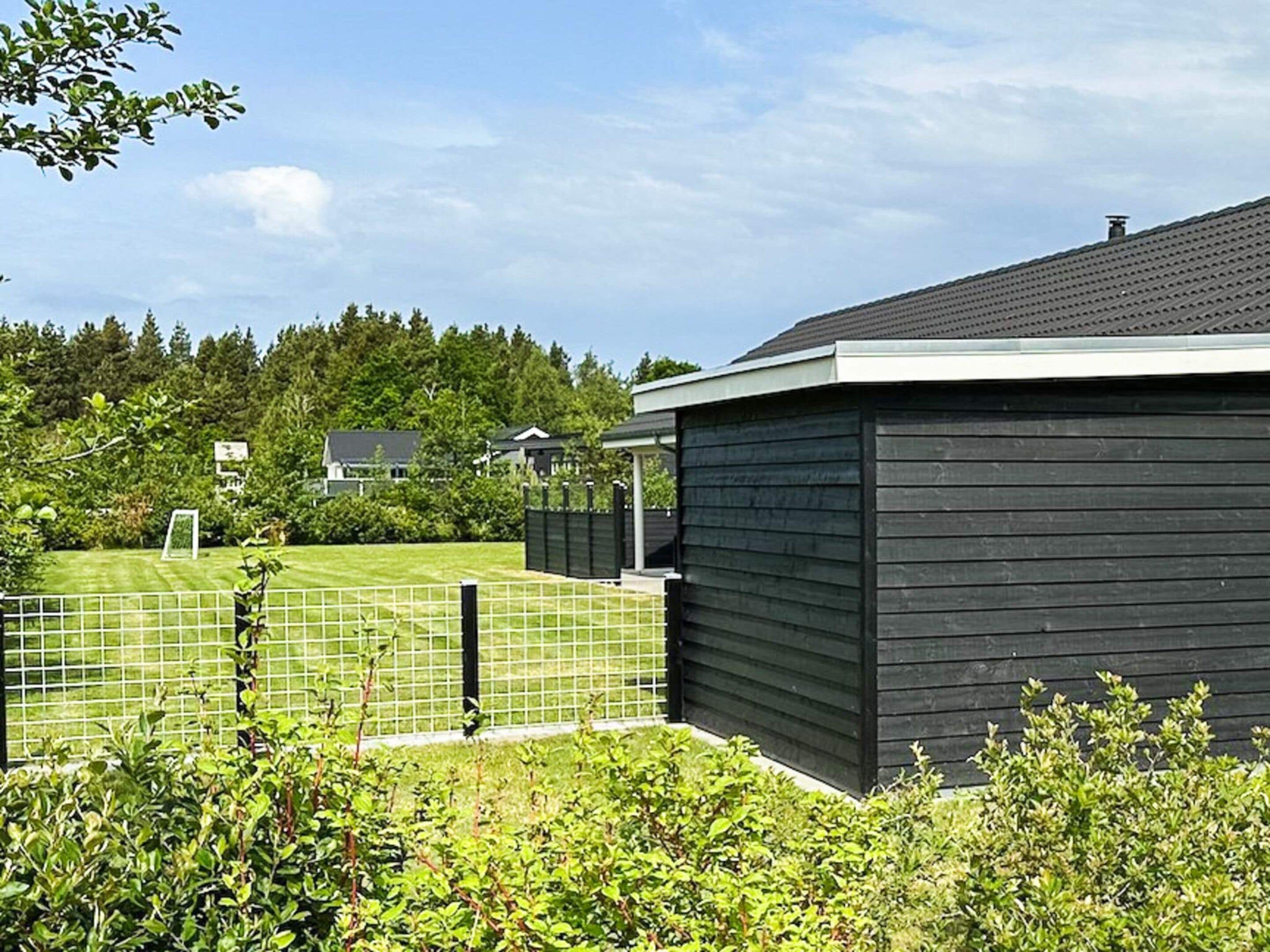 En boligejendom med en indhegnet have, et mørkt træskur og et hus i baggrunden.