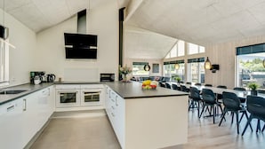 A modern kitchen with a central island, built-in ovens, and a dining area with chairs and tables. - 5 Star Holiday Home in Norre Nebel (Norre Nebel)