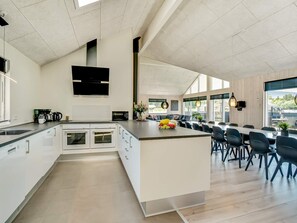 A modern kitchen with a central island, built-in ovens, and a dining area with chairs and tables. - 5 Star Holiday Home in Norre Nebel (Norre Nebel)