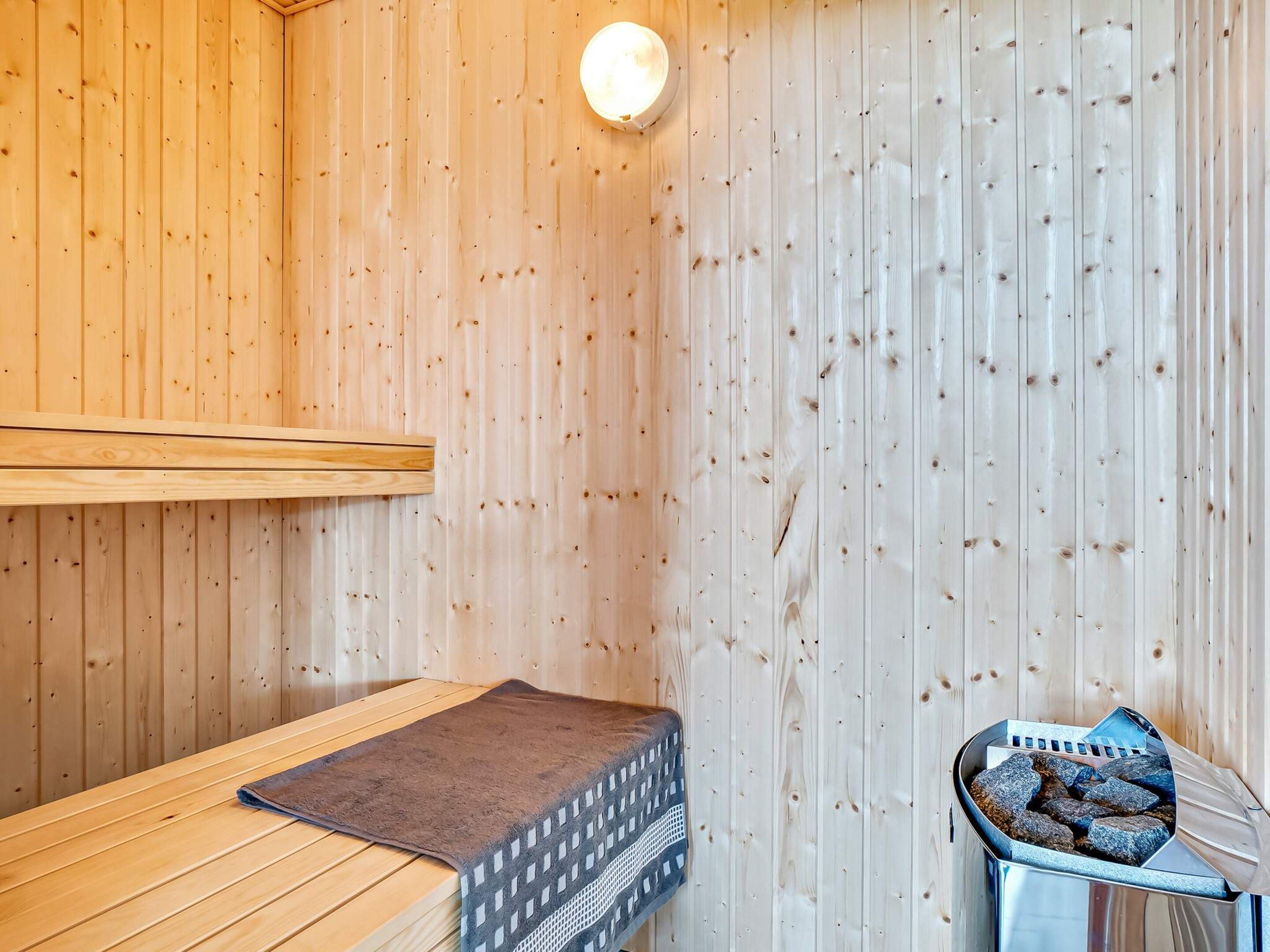 Un sauna avec des murs en bois, un banc, un coussin pour le banc et un appareil de chauffage.