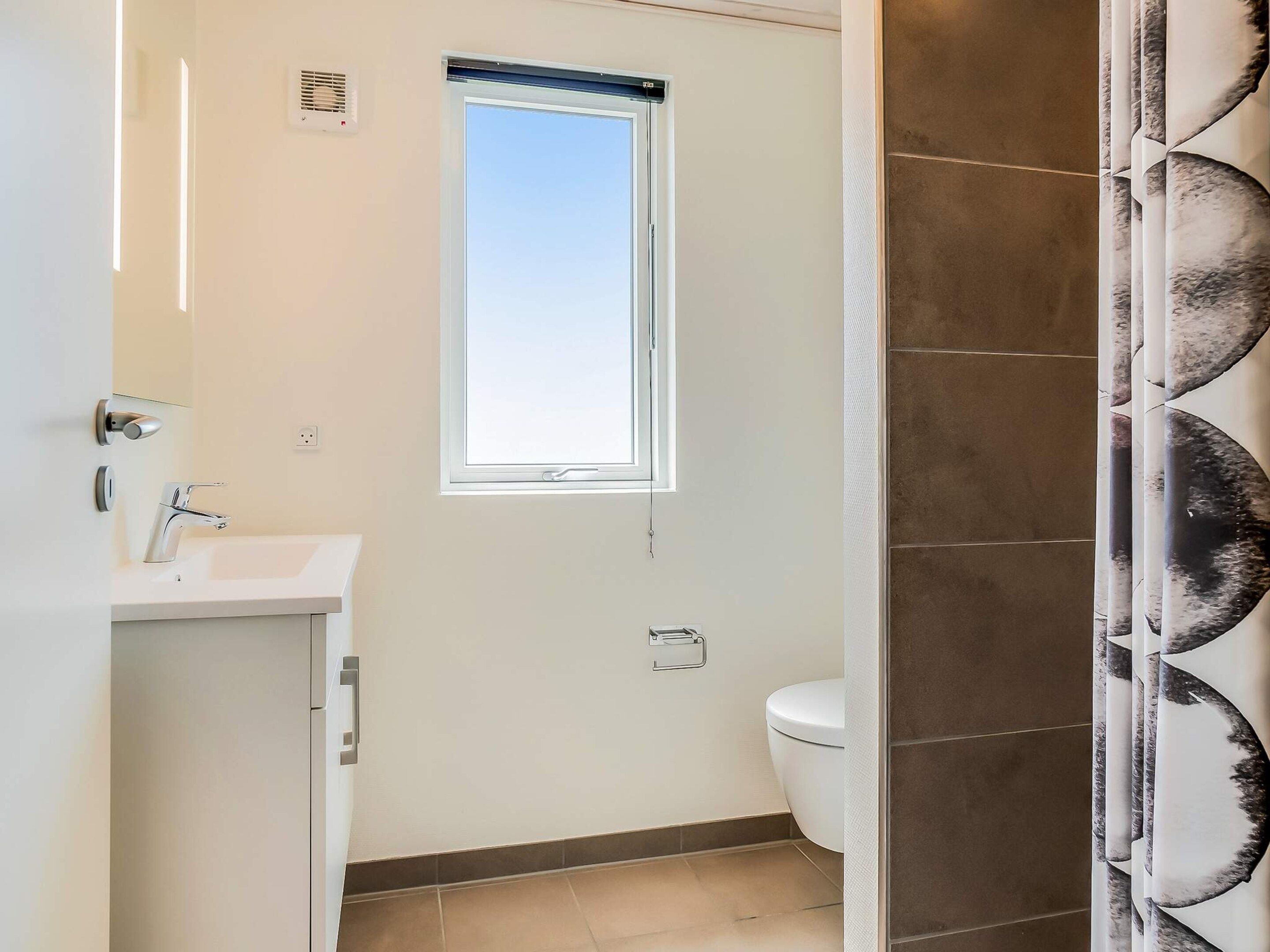 A bathroom with a toilet, a sink, a window, and a shower curtain.