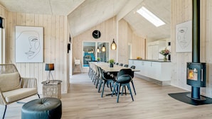 A modern interior with wooden panel walls, a dining area with chairs and a table, a sofa, a small side table, and a fireplace. - 5 Star Holiday Home in Norre Nebel (Norre Nebel)