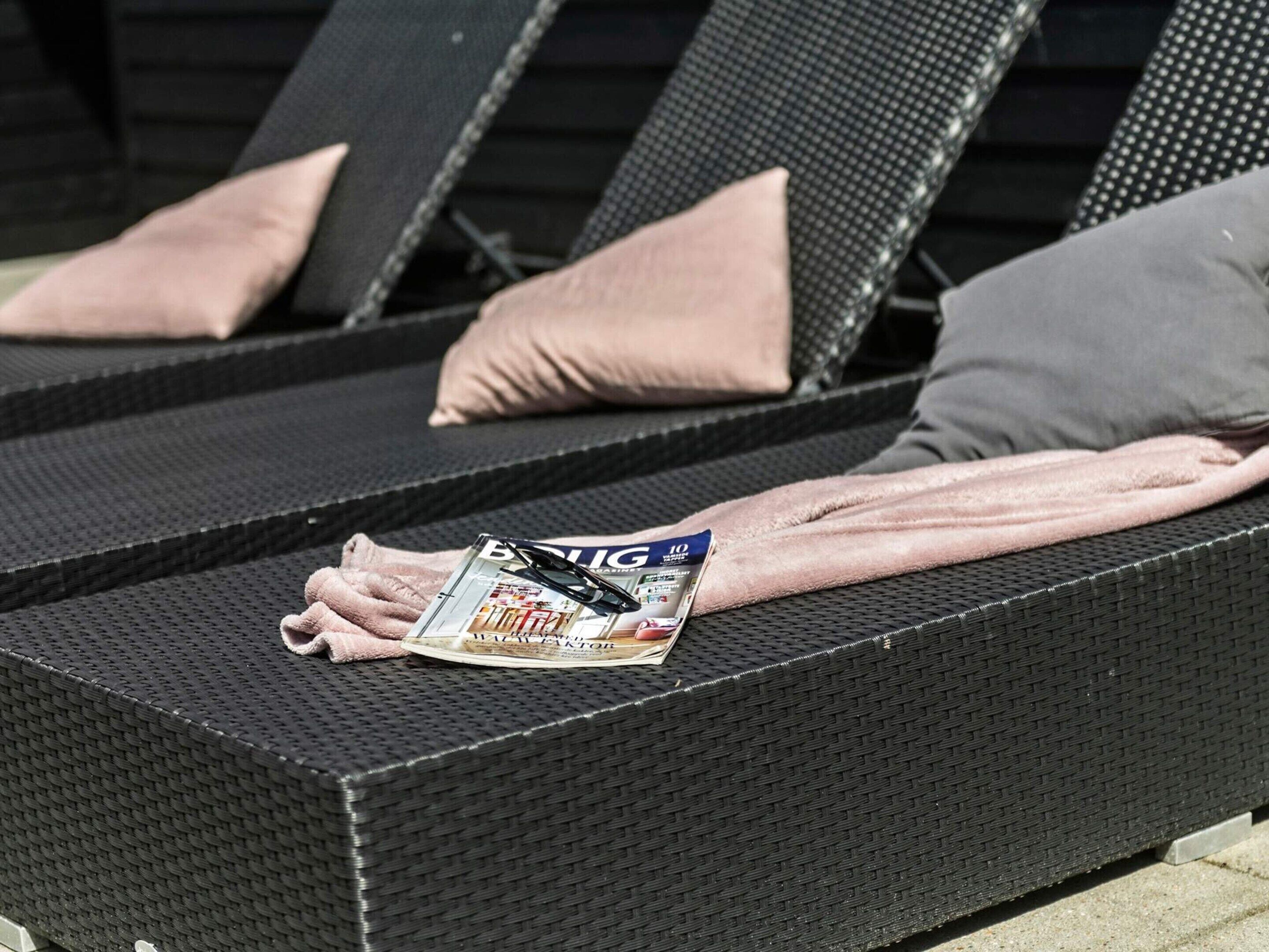 A lounge chair with a magazine, pillows, and a towel.