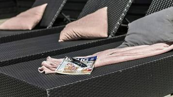 A lounge chair with a magazine, pillows, and a towel.