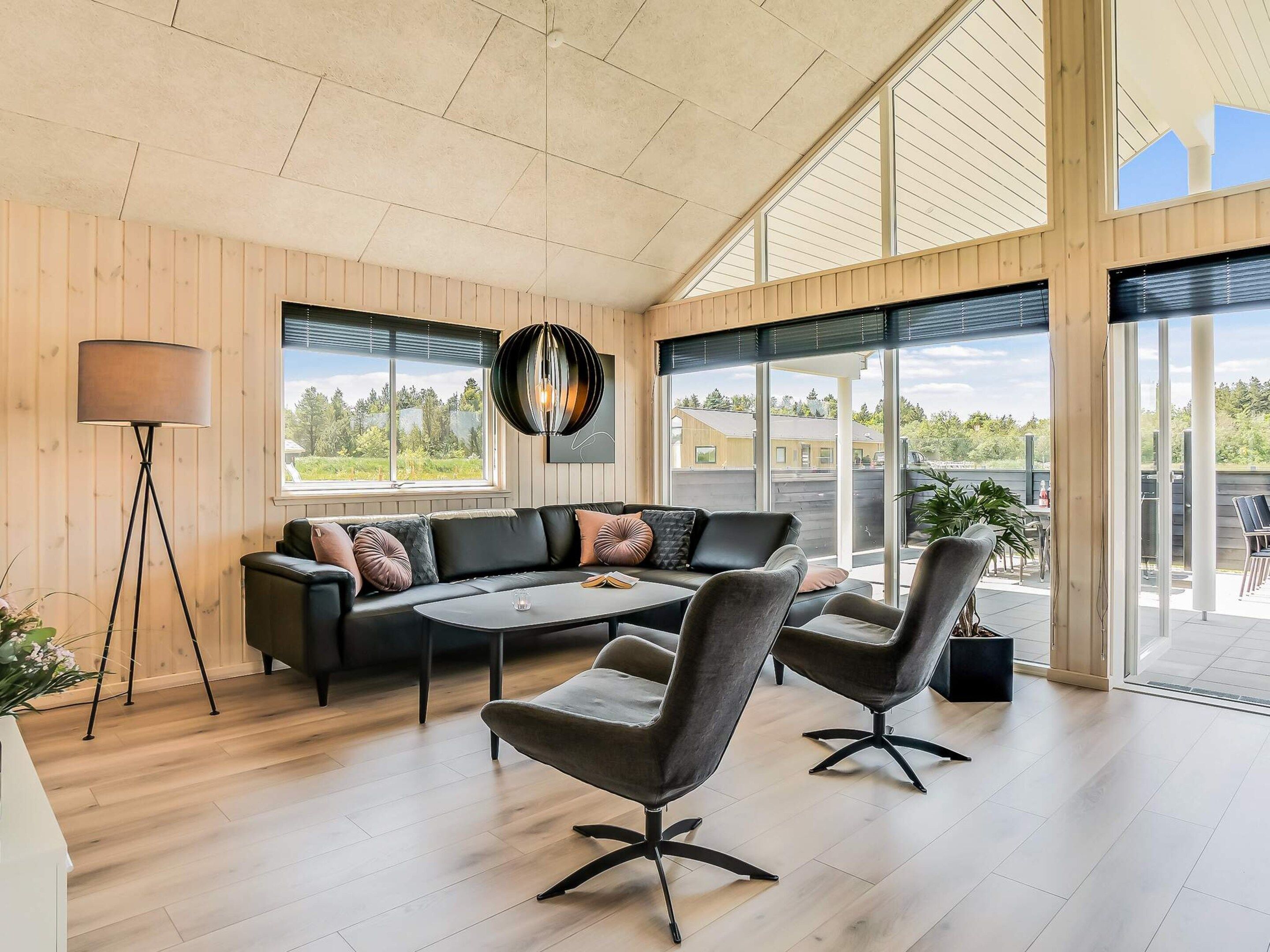 A modern living room with a sectional sofa, two armchairs, a coffee table, and a floor lamp. Large windows provide a view of the outdoors.