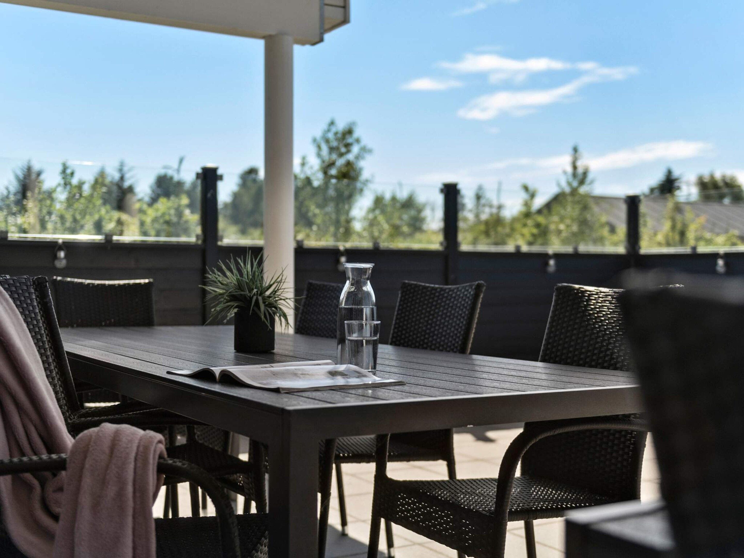 An outdoor patio with a table and chairs, a potted plant, and a clear view of trees and sky.