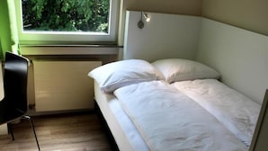 Una habitación pequeña con cama individual, ventana, silla y radiador.
