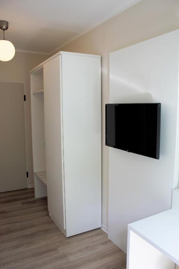 A room with a white wardrobe, a flat-screen TV mounted on the wall, and a wooden floor. - Bendorf Hotel by Belvilla Budget Double Room (Bendorf)