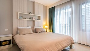 A hotel room with a bed, bedside table, lamp, and a window with curtains. - Quiet Comfor Room, near Central Mall (Tambon Patong)