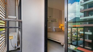 Un dormitorio con cama, mesita de noche, lámpara y vistas a un balcón con barandilla.