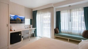 Habitación de hotel con cama, escritorio con computadora, televisor montado en la pared y ventana con cortinas.