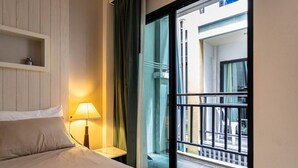 Une chambre d’hôtel avec un lit, une lampe de chevet, une fenêtre donnant sur la rue et un balcon avec une balustrade.