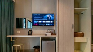 Une chambre d’hôtel compacte dotée d’un téléviseur à écran plat fixé au mur, d’une petite kitchenette avec un réfrigérateur, d’une chaise blanche et d’une poubelle.