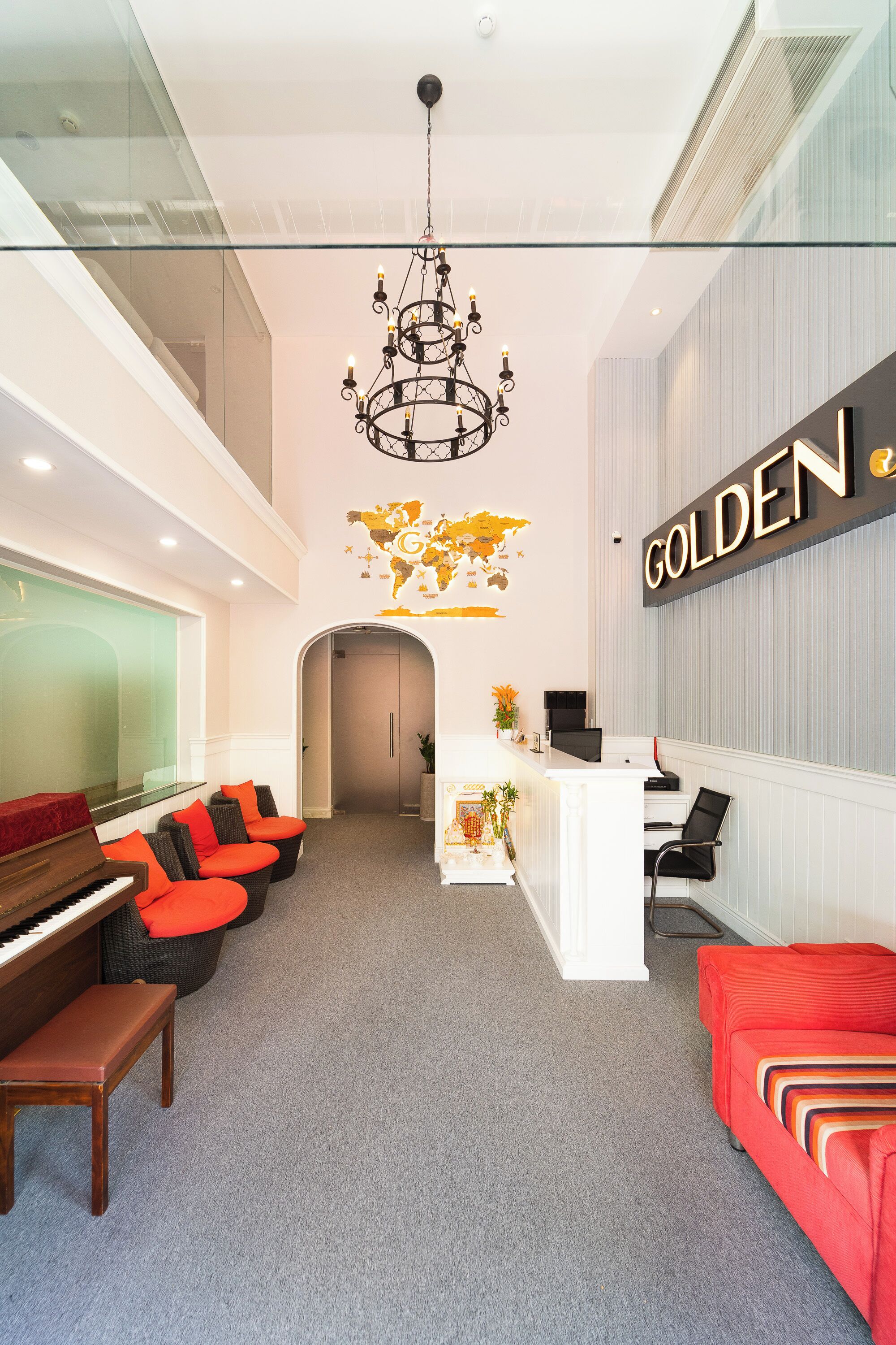 A reception area with a piano, seating, a chandelier, a reception desk, and a wall-mounted sign.