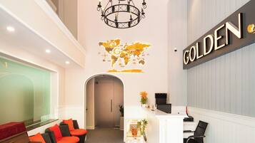 A reception area with a piano, seating, a chandelier, a reception desk, and a wall-mounted sign.