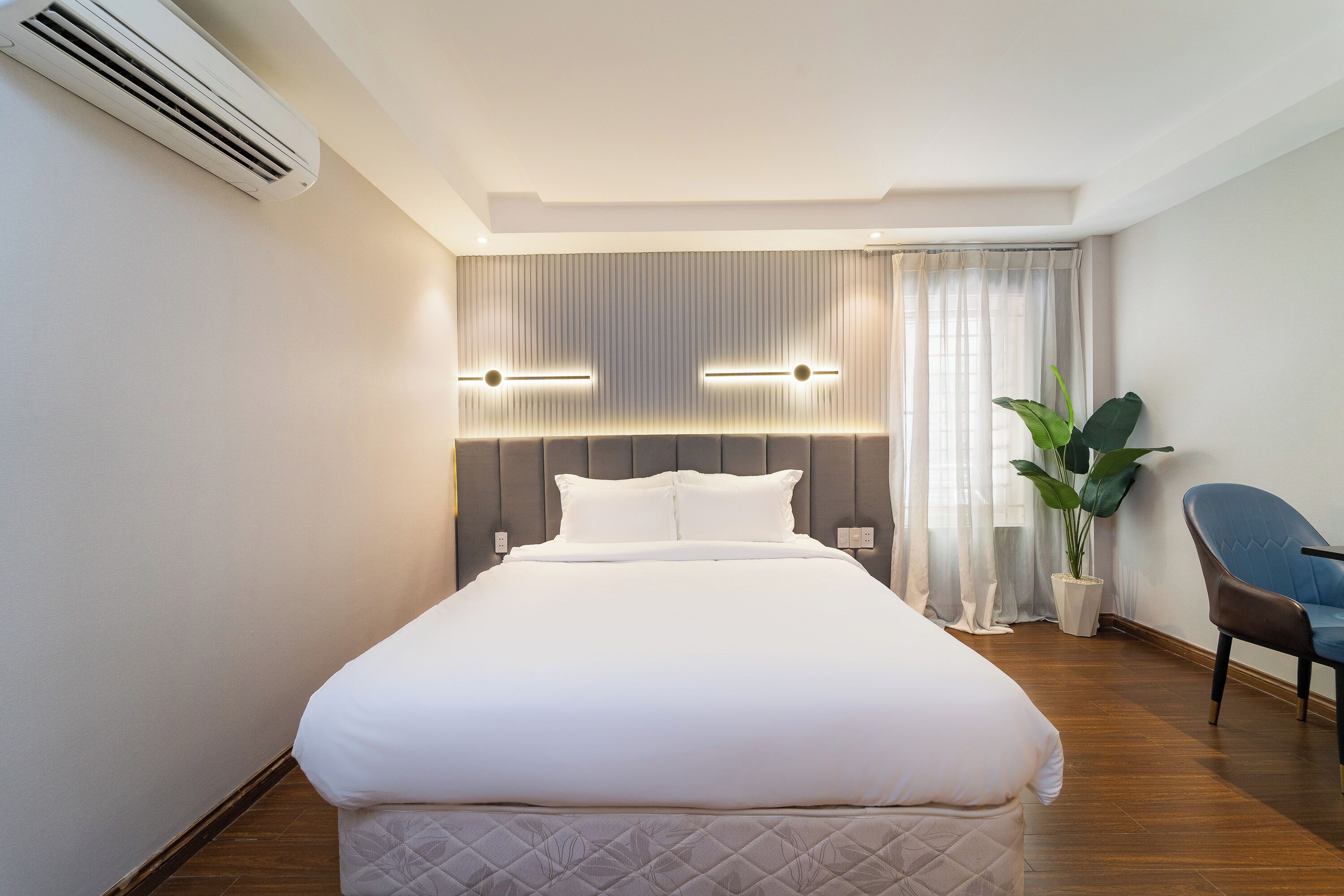 A hotel room with a bed, a potted plant, a chair, and a wall-mounted air conditioner.