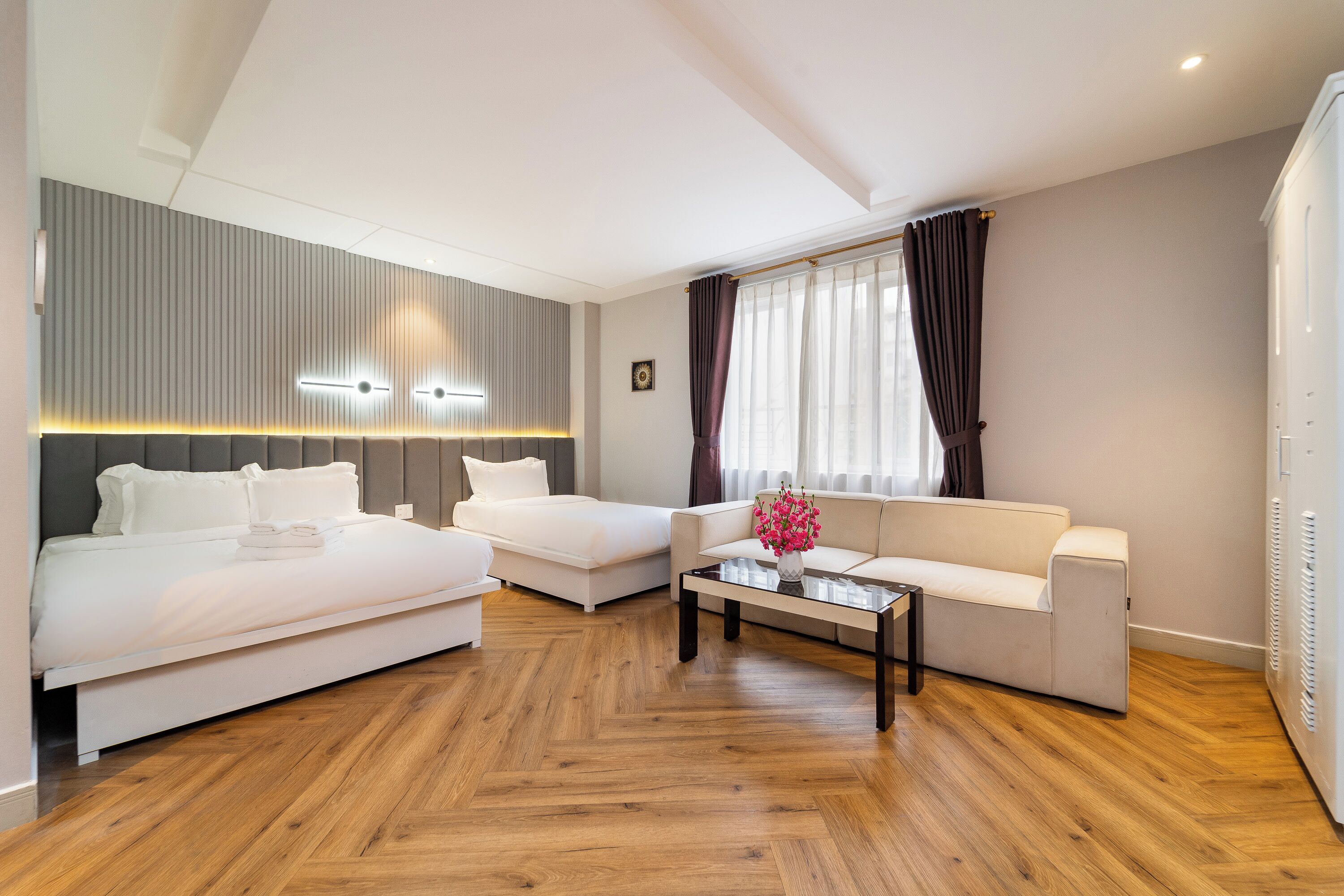 Una habitación de hotel moderna con cama, sofá, mesa de centro y un amplio ventanal con cortinas.