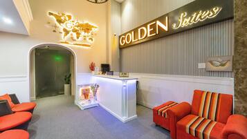 Ein Empfangsbereich mit einem 'GOLDEN Suites' Schild, einem Empfangstisch, einer Weltkarte als Dekoration und einer Rezeption.