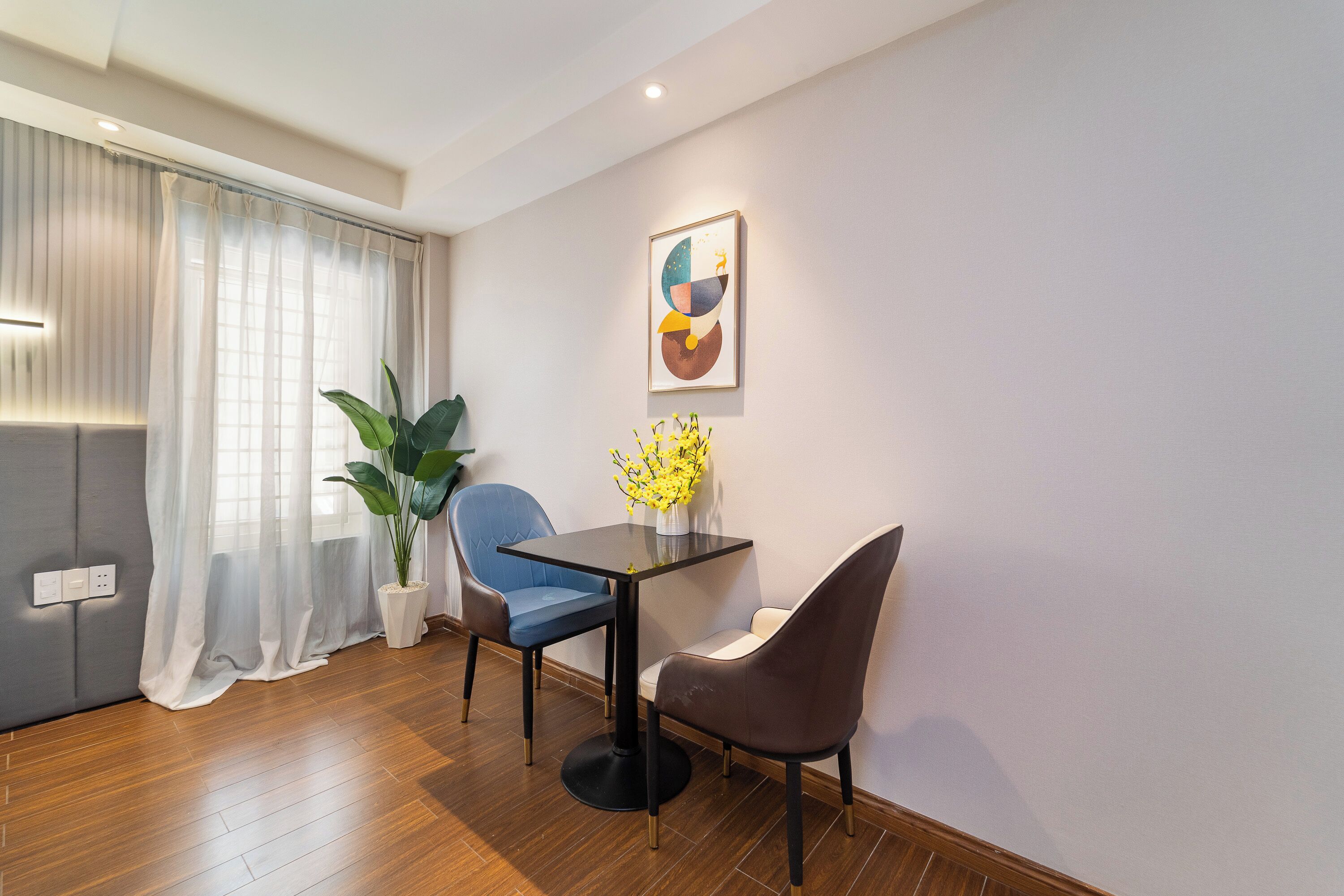A modern dining area with a table, two chairs, a potted plant, and a wall-mounted artwork.