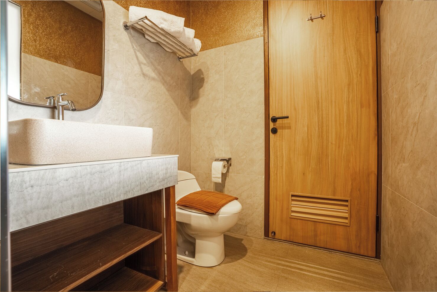 A bathroom with a sink, mirror, toilet, and wooden door.