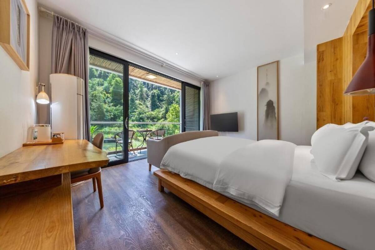 Ein Schlafzimmer mit Bett, Schreibtisch, Stuhl, Fernseher und einer Schiebetür zum Balkon.