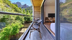 A balcony with a view of a mountainous landscape, a dining area with a table and chairs, and a bedroom with a bed and a TV. - Avatar Peaks Resort (Zhangjiajie)