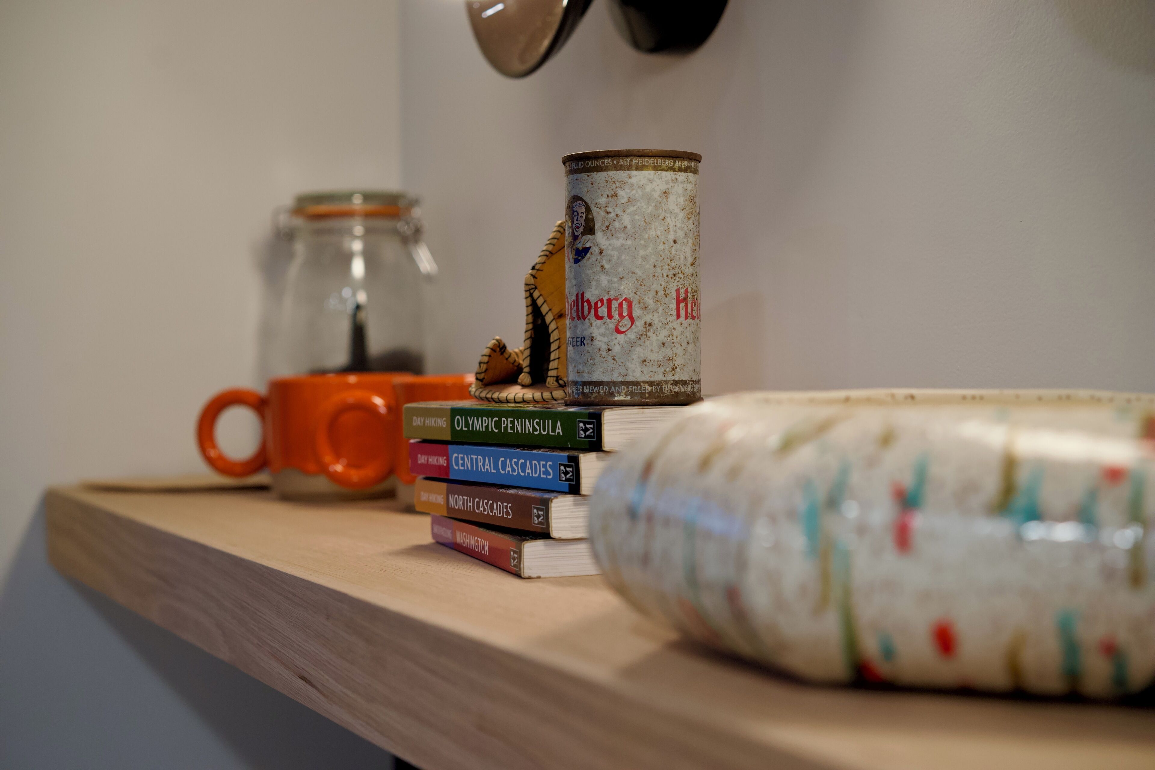 Una repisa con libros, una lata, una taza y un adorno.