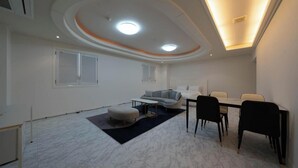 Een moderne woonkamer met een bank, een poef, een eettafel, stoelen en inbouwspots.