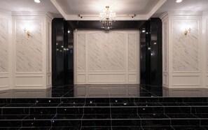 A spacious lobby with marble walls, a chandelier, and a staircase leading to an upper level.