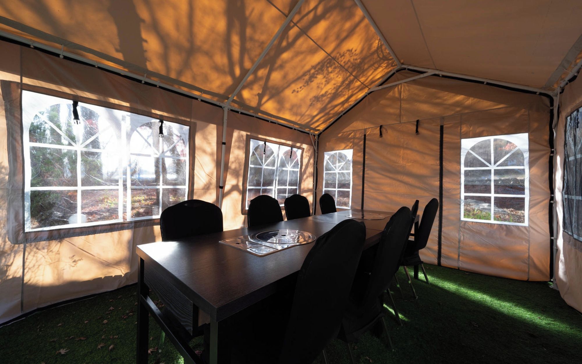 A tent with a dining table and chairs, large windows, and a grassy floor.
