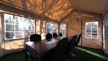 A tent with a dining table and chairs, large windows, and a grassy floor.
