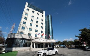 A hotel with a modern facade, multiple flags, and a parking lot with a white car.