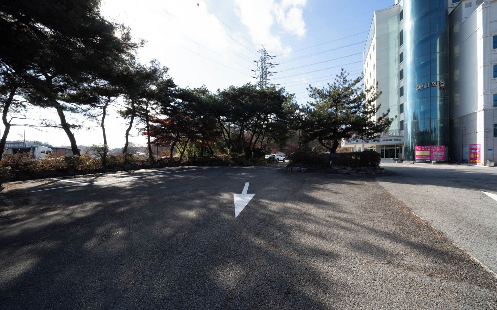 A road with a white arrow pointing straight ahead, surrounded by trees and a building with a glass facade.