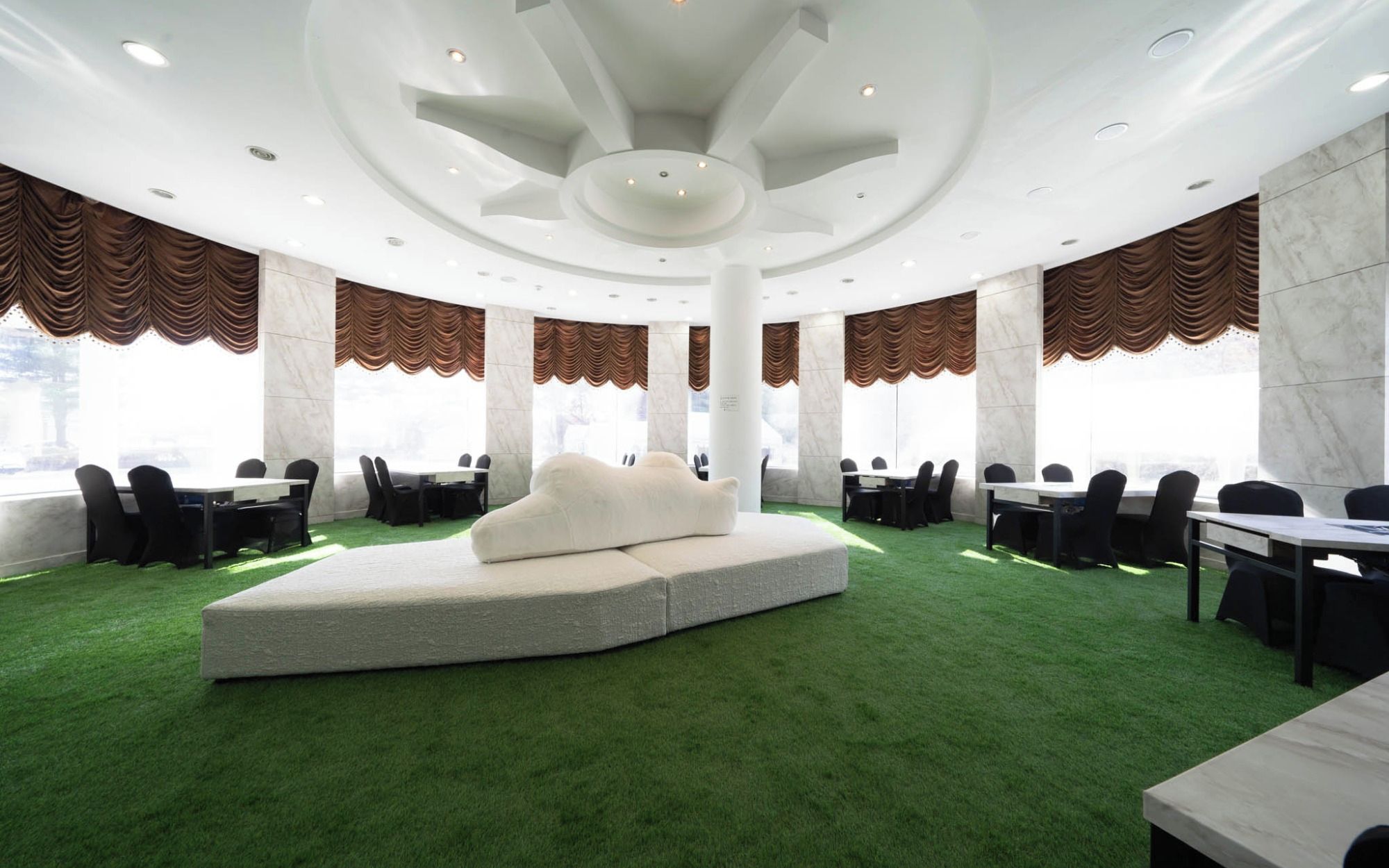 A conference room with a central seating area, multiple tables, and large windows with curtains.