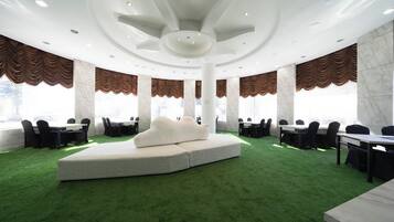 A conference room with a central seating area, multiple tables, and large windows with curtains.