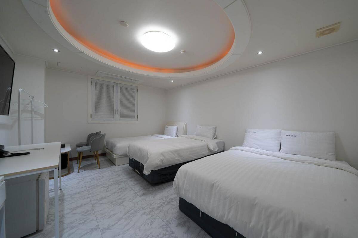 A bedroom with two beds, a desk, a chair, and a window with blinds.