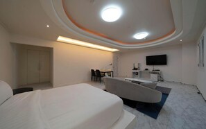 Une chambre d’hôtel moderne équipée d’un lit, d’un coin salon avec des fauteuils, d’un bureau, d’un téléviseur à écran plat et d’un plafond doté d’un éclairage encastré.