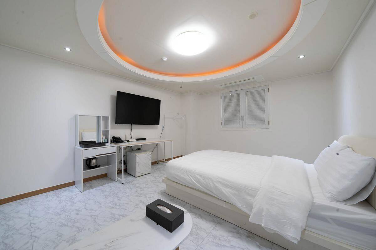A modern hotel room with a bed, a desk, a television, and a ceiling light.