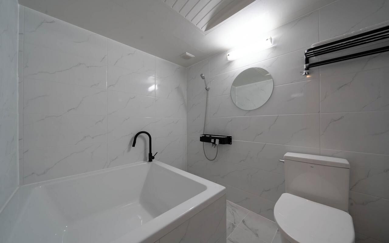 Un baño con una bañera blanca, un inodoro, una ducha y un espejo redondo en la pared.
