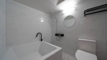 Un baño con una bañera blanca, un inodoro, una ducha y un espejo redondo en la pared.