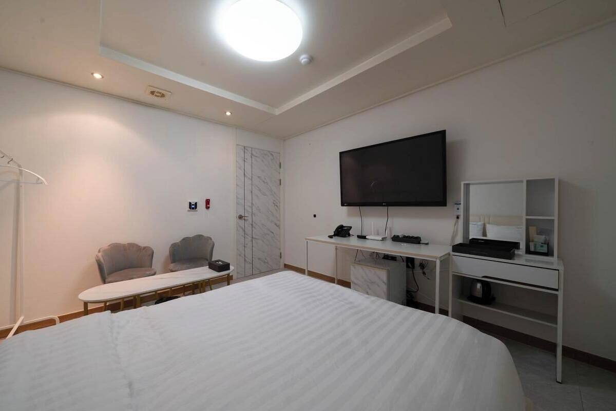 A hotel room with a large bed, a desk with a computer, a flat-screen TV, a chair, and a wardrobe.