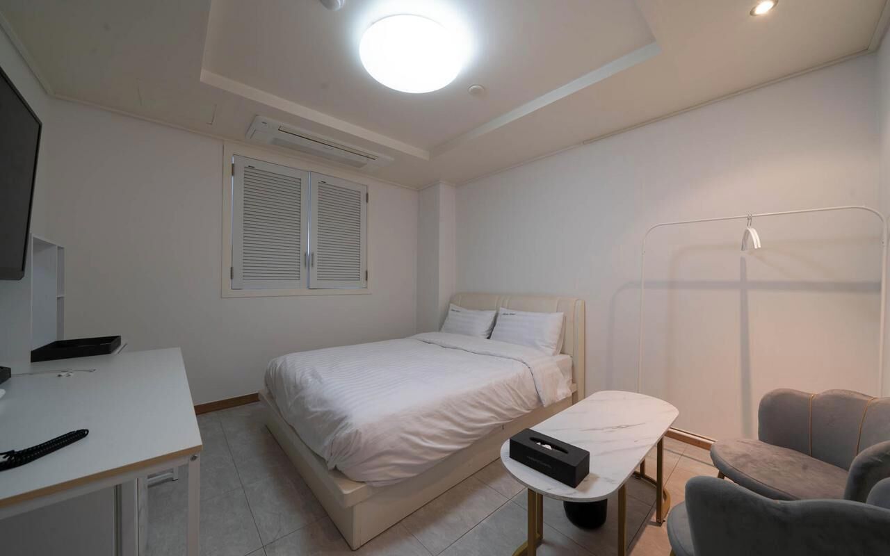 Un dormitorio con cama, mesita de noche, escritorio, silla y zona de ducha.