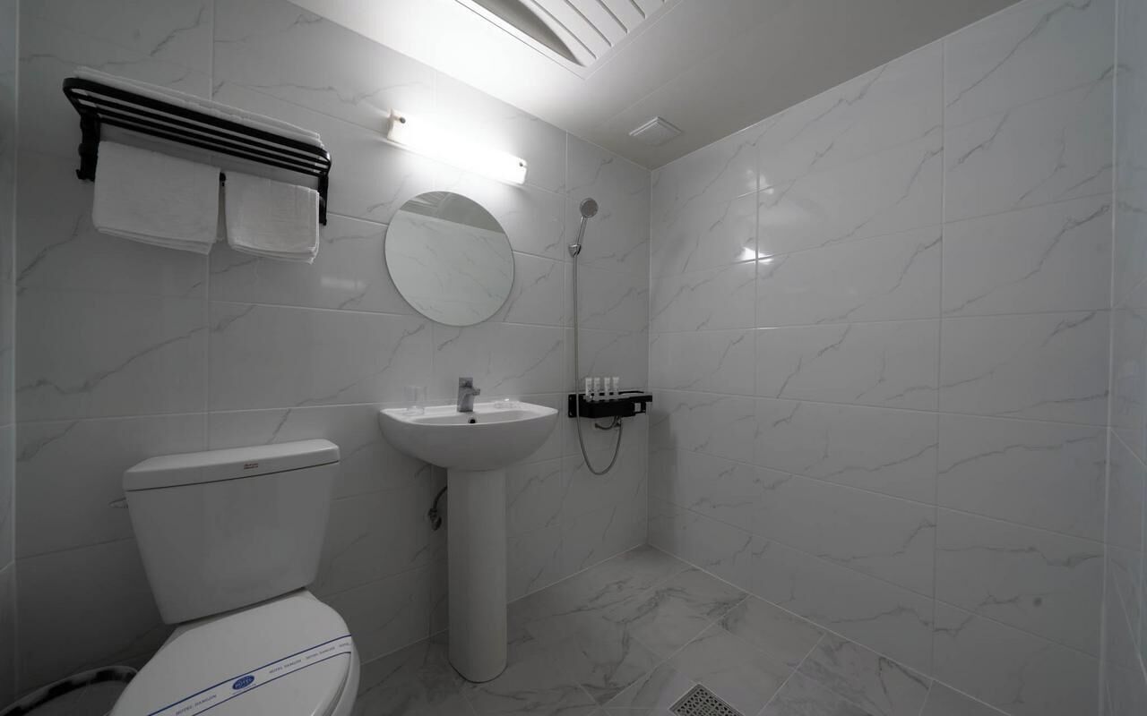 A bathroom with a toilet, sink, mirror, towel rack, and shower.