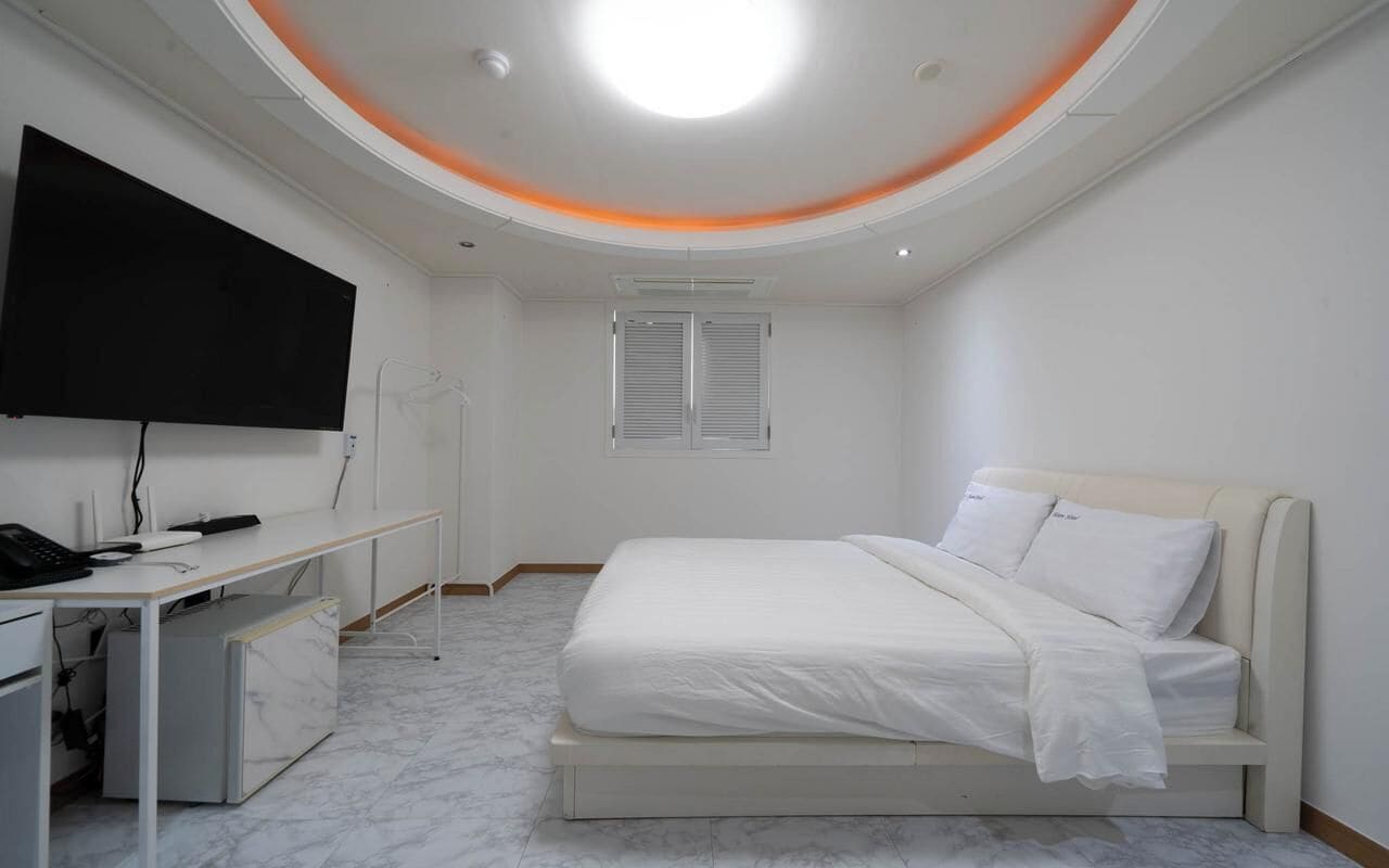 Un dormitorio con cama, escritorio, televisor y ventana con contraventanas.