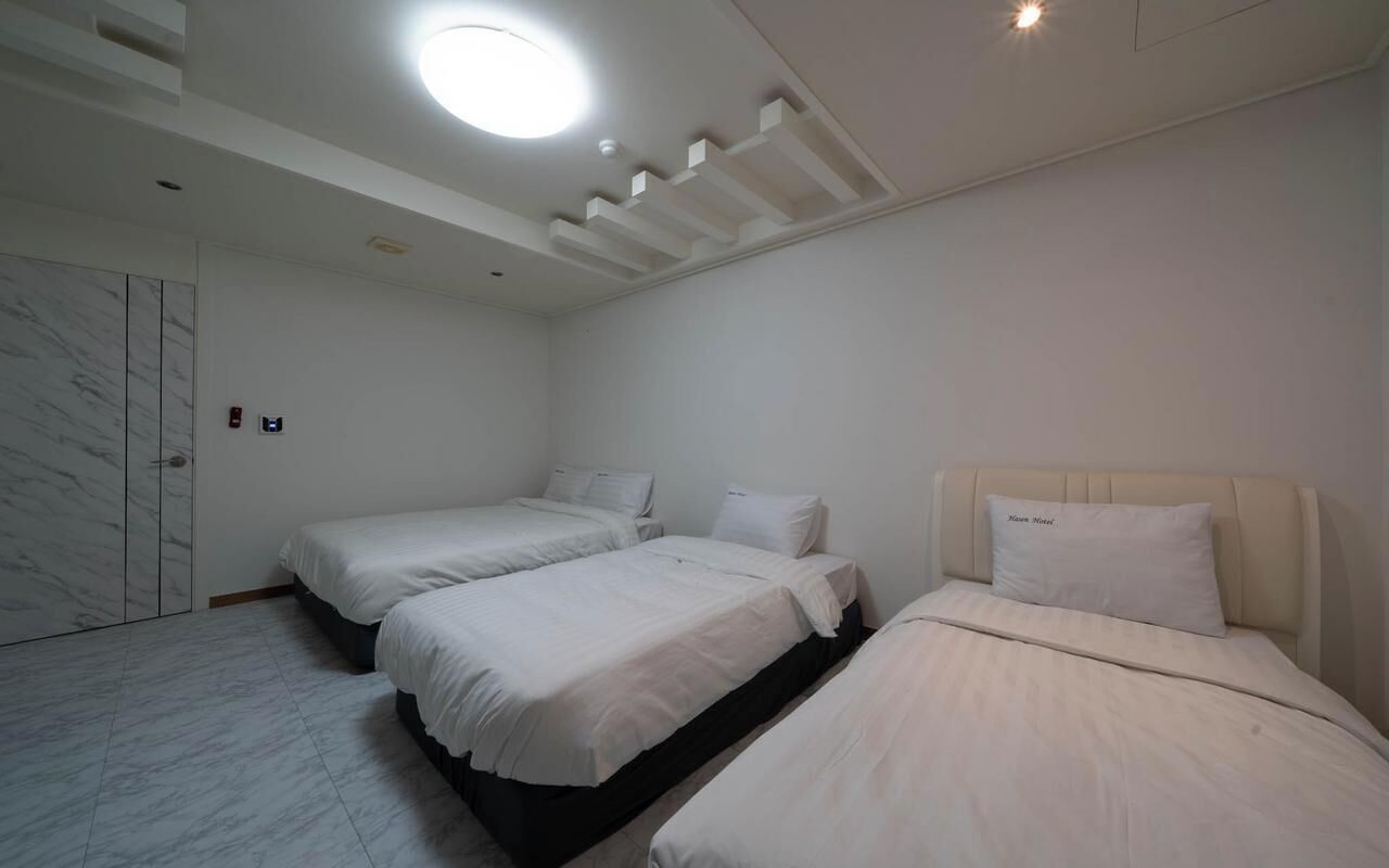 A hotel room with three beds, a marble floor, a ceiling light, and a door with a handle.