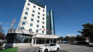 Een hotel met een moderne glazen gevel, een parkeerplaats en een witte auto ervoor geparkeerd.