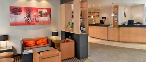 Eine Hotelhalle mit Rezeption, einer Sitzecke mit Sofas und Sesseln, einem großen abstrakten Gemälde an der Wand und einem Teppichboden.